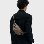 JONES + CO Bon-Bon taupe leather shoulder bag with metal clasp worn across the back by a person in a black jacket