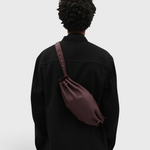 JONES + CO Bon-Bon M wine leather crossbody bag worn by a person in a black jacket, showing back view
