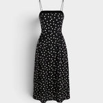 A black midi dress with a white polka dot pattern, featuring thin spaghetti straps and a fitted bodice, displayed against a light gray background.