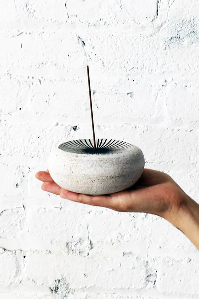 Hand holding a small stone-like incense burner with a white background