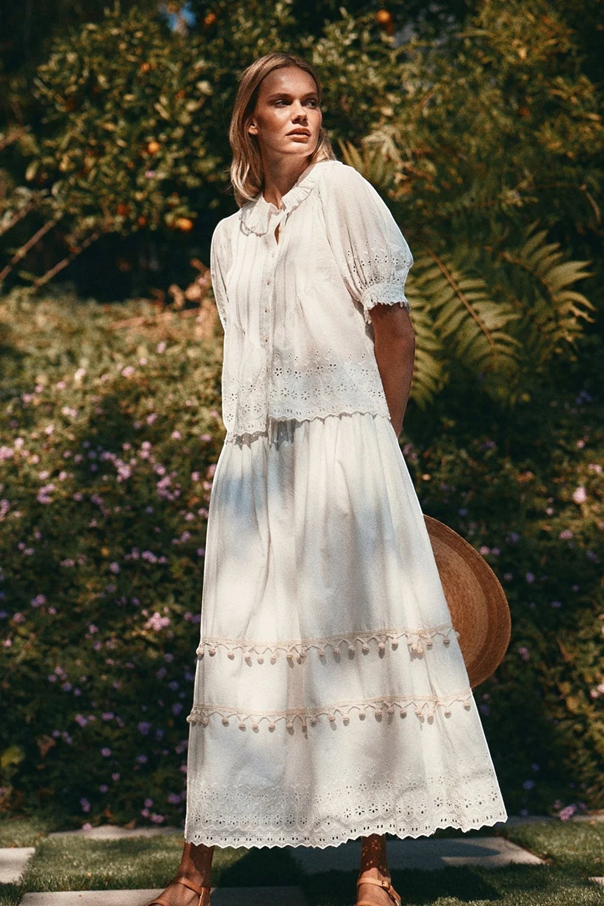 Woman in a white dress standing outdoors with greenery and flowers in the background
