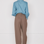 Person wearing a blue shirt and brown pants standing against a white wall.
