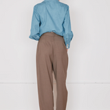 Person wearing a blue shirt and brown pants standing against a white wall.