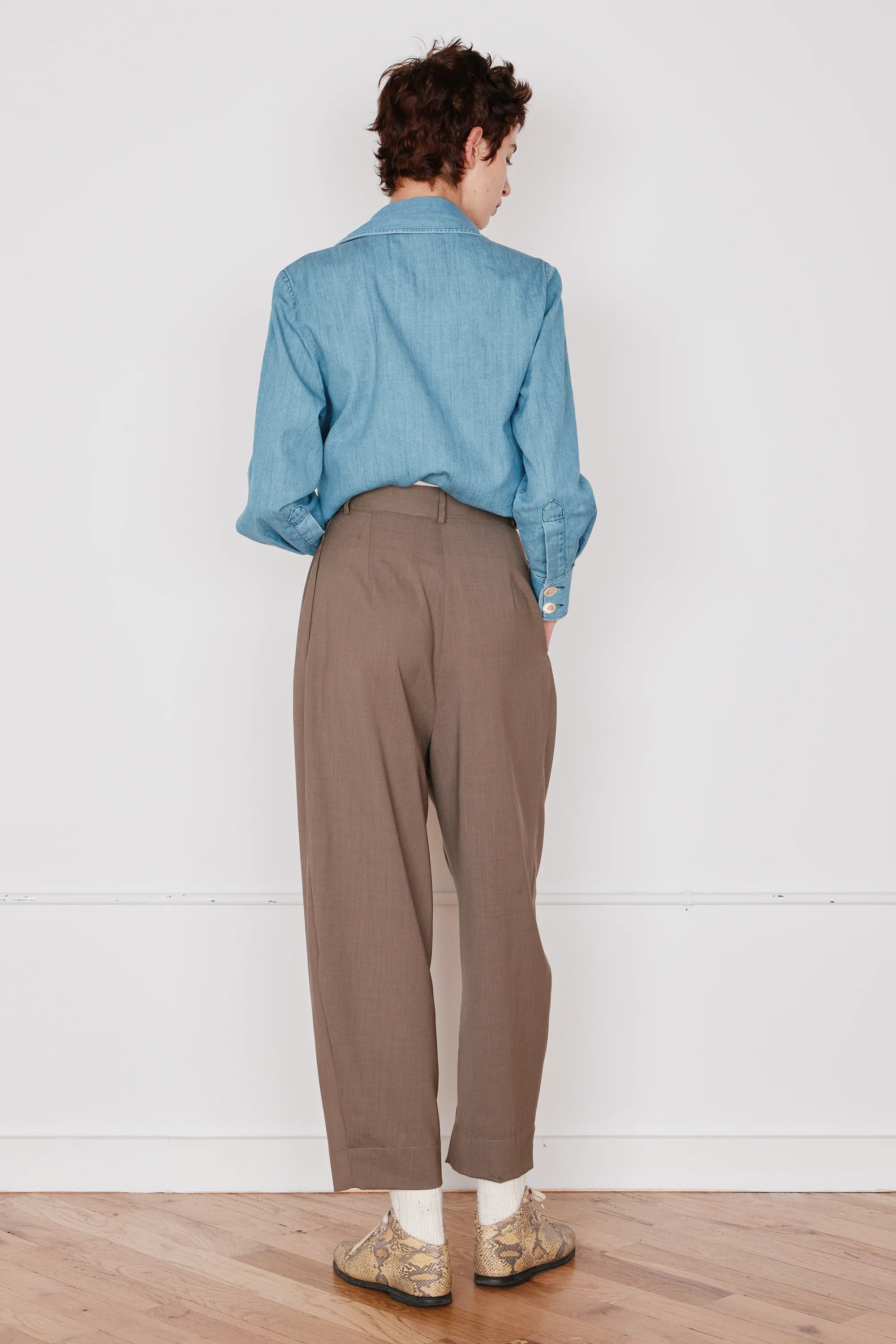 Person wearing a blue shirt and brown pants standing against a white wall.