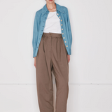Person wearing a blue denim jacket, white shirt, and brown pants on a white background