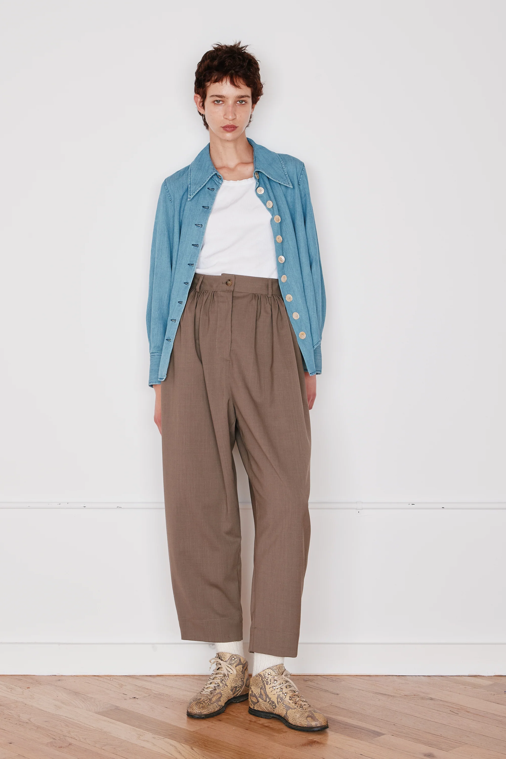 Person wearing a blue denim jacket, white shirt, and brown pants on a white background