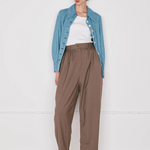 Person wearing a blue denim jacket, white shirt, brown pants, and beige shoes on a white background