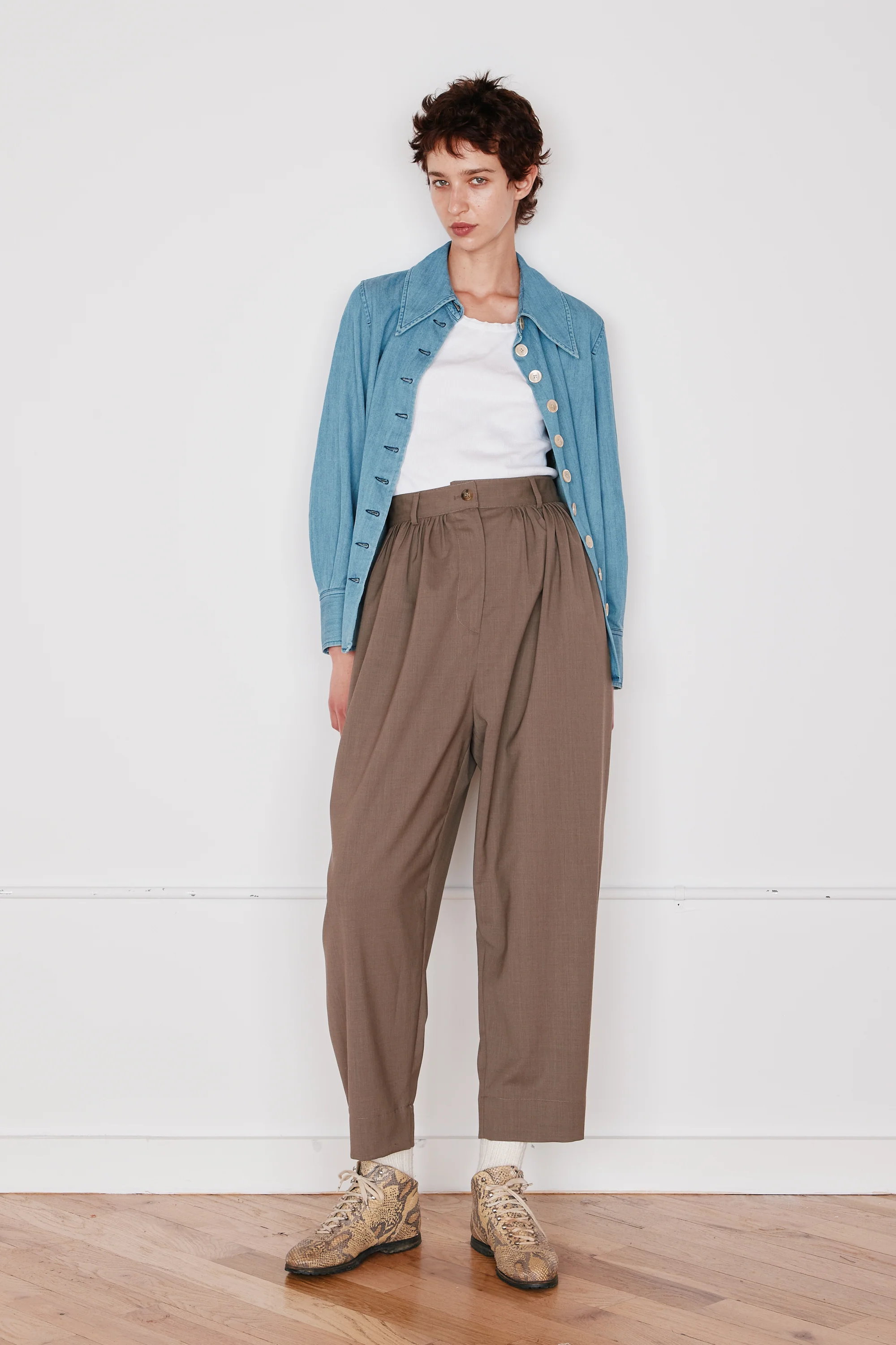 Person wearing a blue denim jacket, white shirt, brown pants, and beige shoes on a white background
