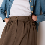 Person wearing a blue denim jacket, white shirt, and brown pants against a plain background