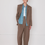 Person wearing a brown suit with a blue shirt against a white wall.