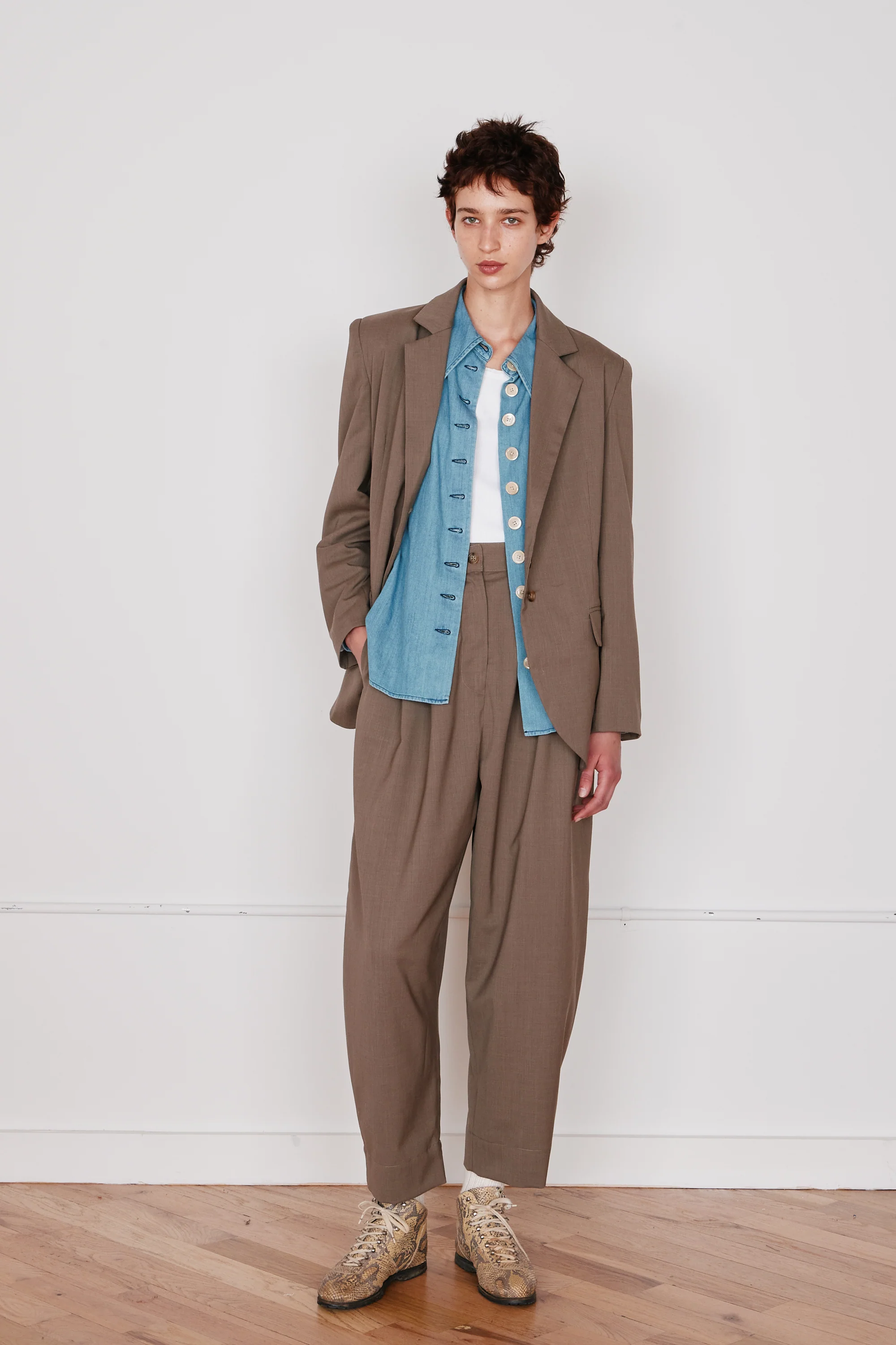 Person wearing a brown suit with a blue shirt against a white wall.