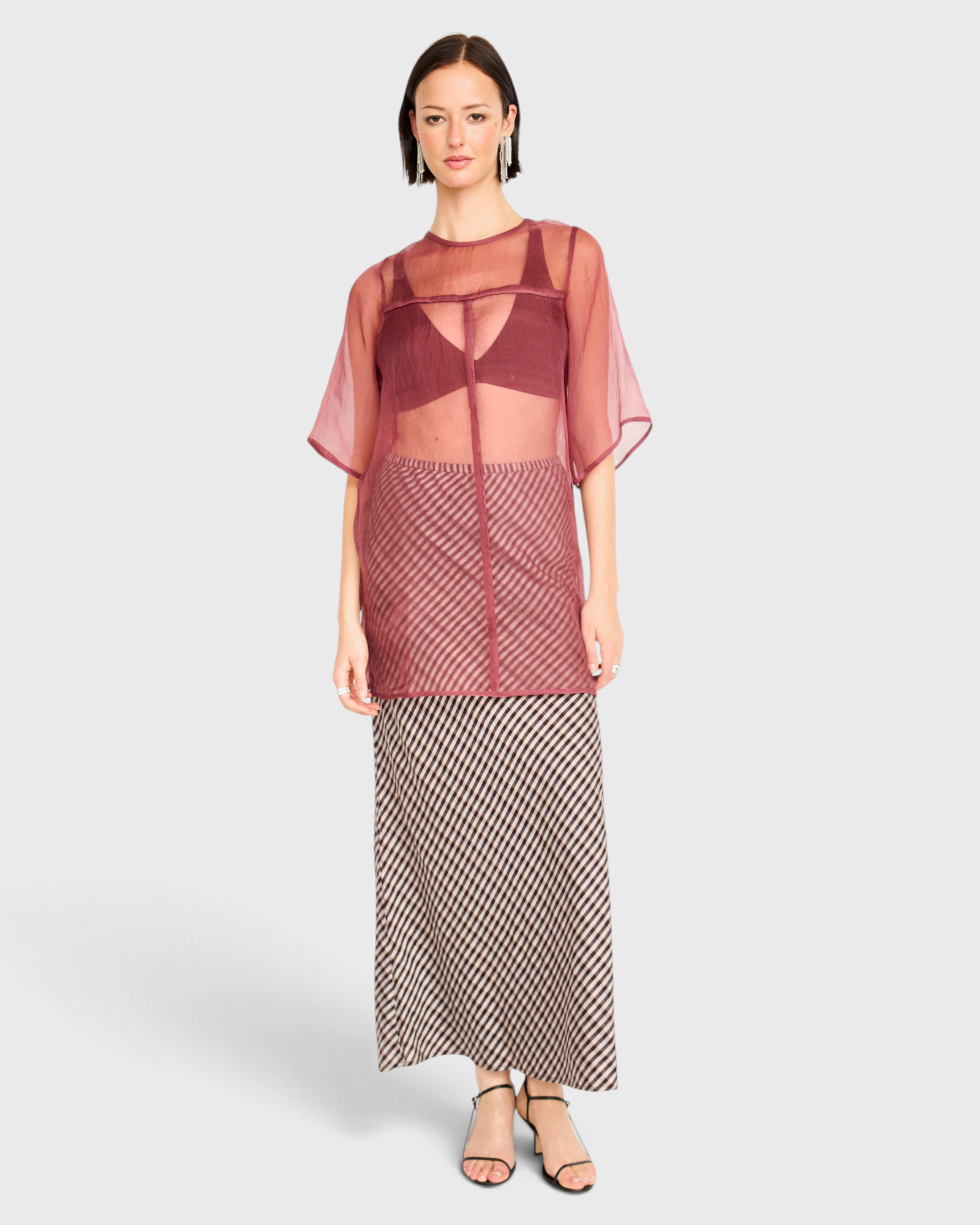 Model wearing JONES + CO Santander silk skirt in shadowline plaid with a sheer burgundy top and black strappy heels.
