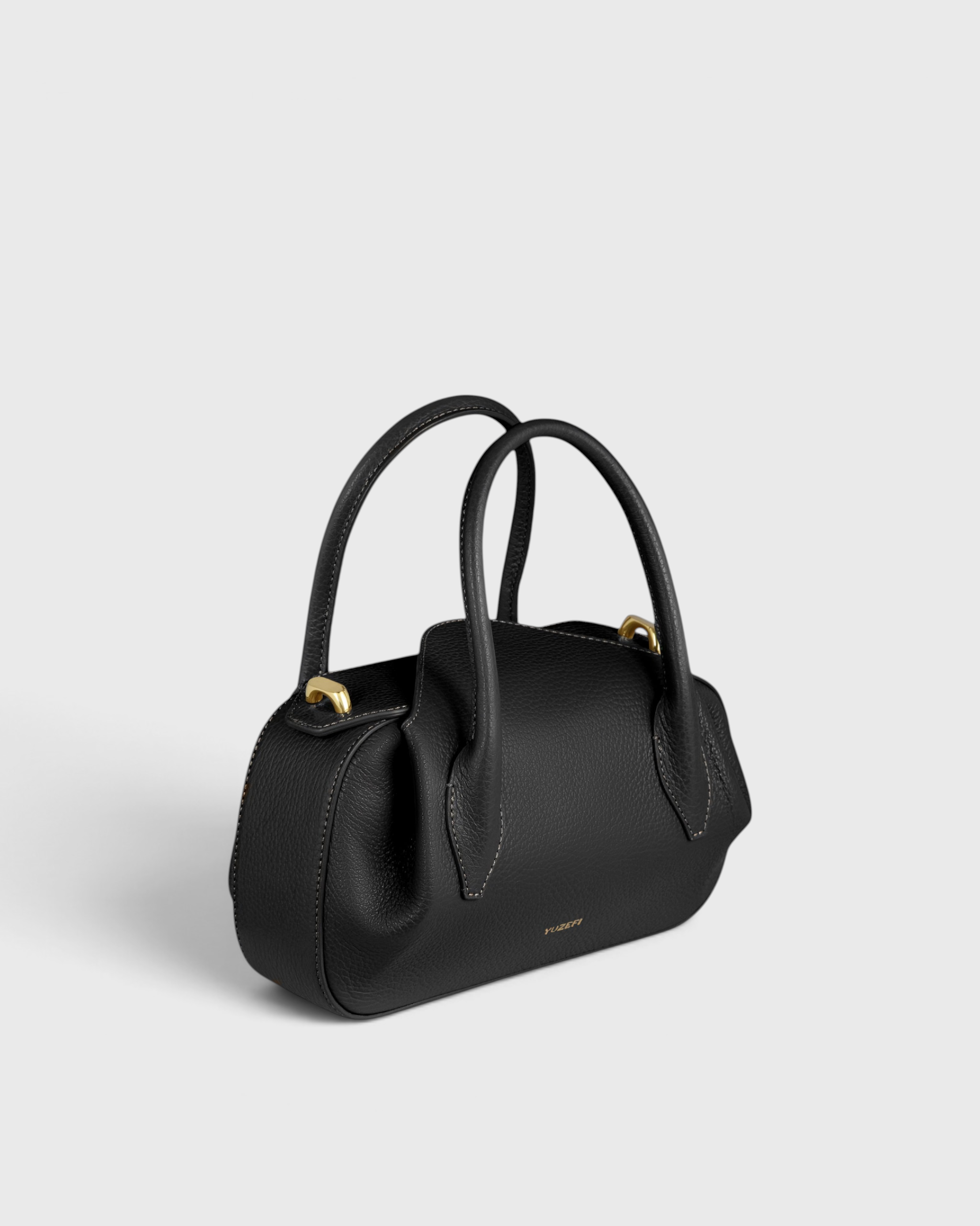 JONES + CO Oyster Mini Duffle in black pebble grained Italian leather with gold-tone hardware and top handles.