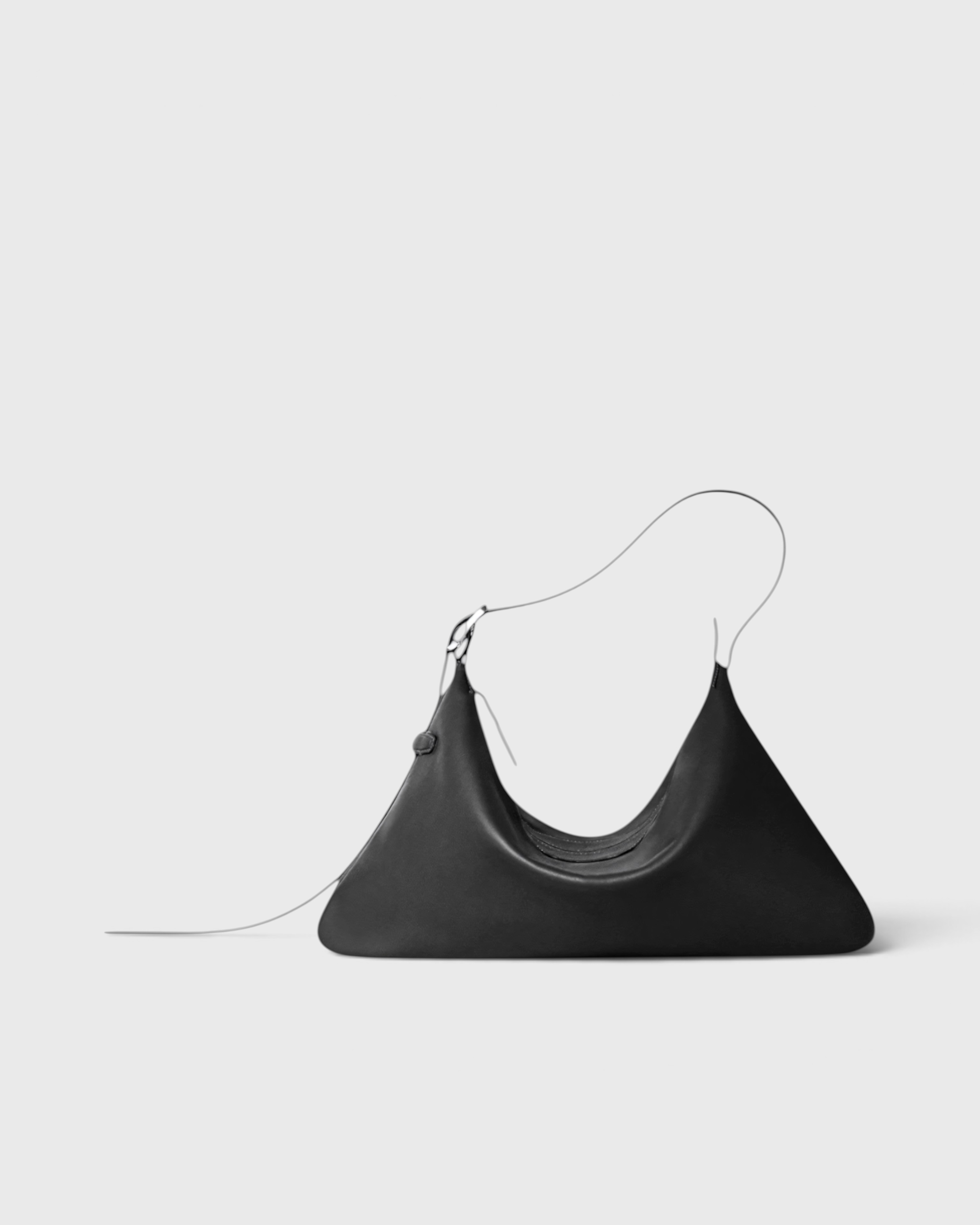 JONES + CO Rider M black leather shoulder bag with a unique skateboard rink shape and adjustable belt-style strap.