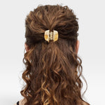 Person with wavy hair tied back with a decorative hair clip on a white background