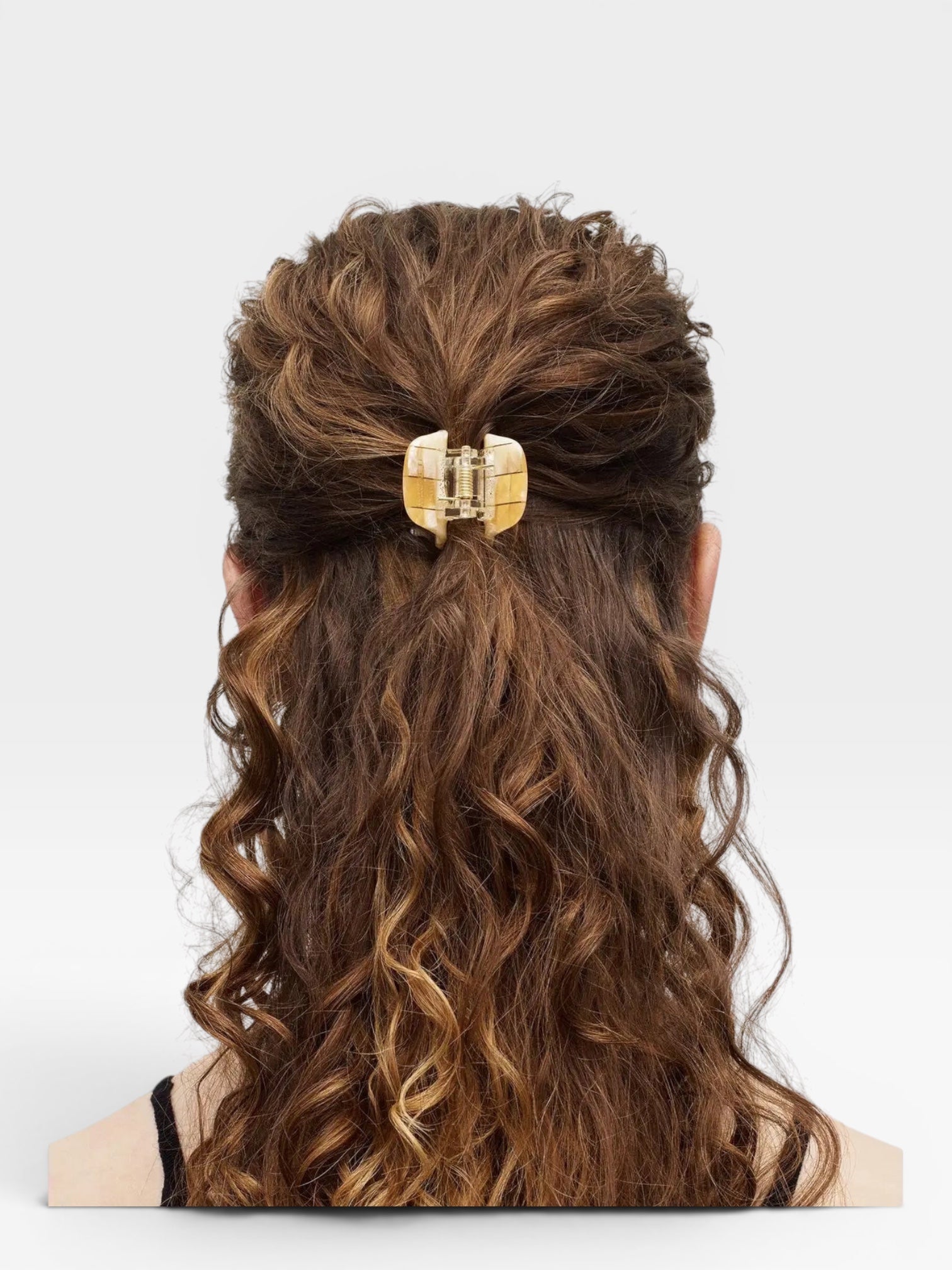 Person with wavy hair tied back with a decorative hair clip on a white background