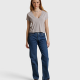 Model wearing JONES + CO cloud gray recycled cotton Alanis V-neck cropped tee with blue jeans against a draped backdrop