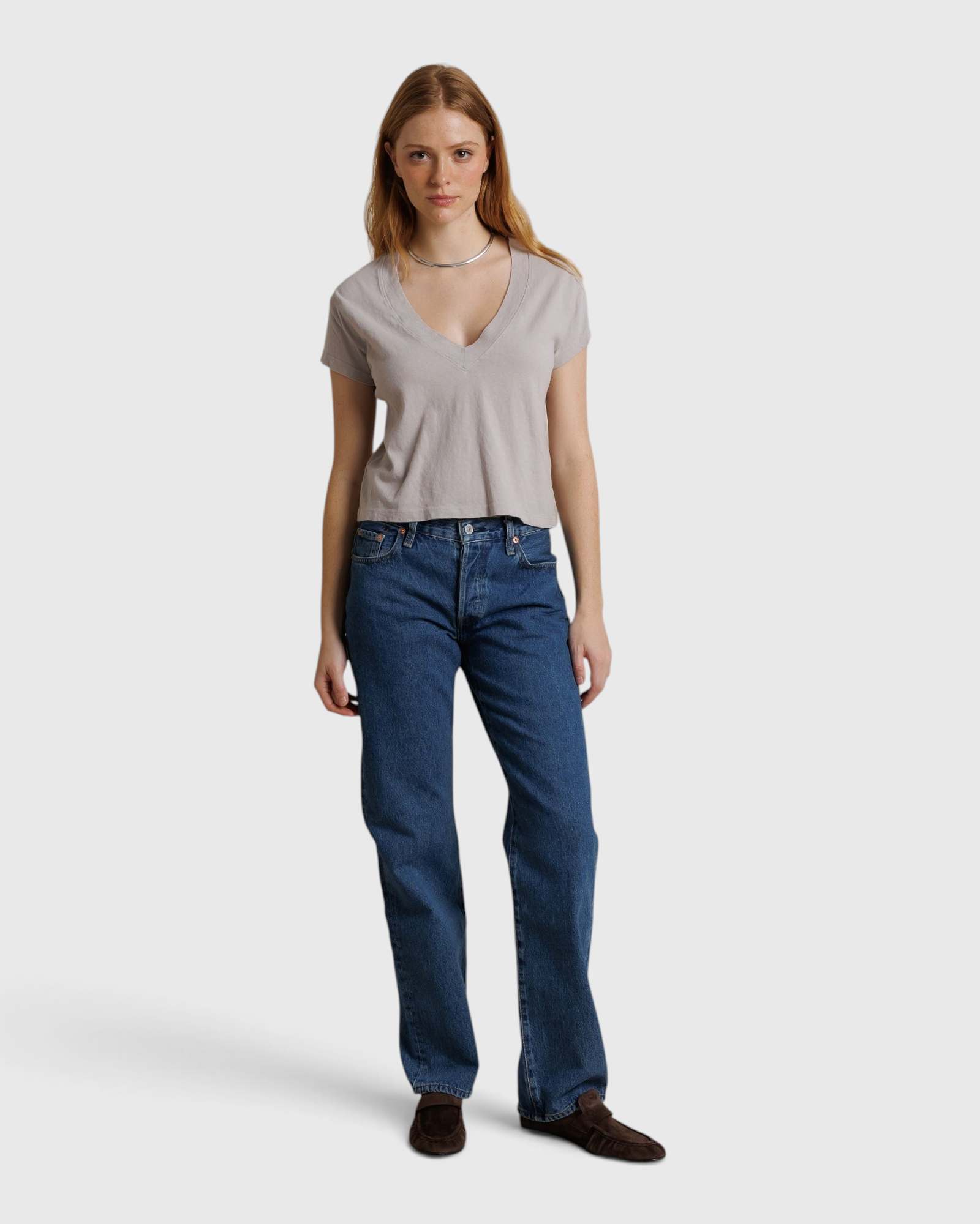 Model wearing JONES + CO cloud gray recycled cotton Alanis V-neck cropped tee with blue jeans against a draped backdrop