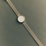Silver watch with a textured band on a green background