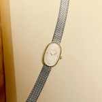 Vintage-style watch with a gold face and silver mesh strap on a beige background