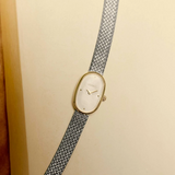 Vintage-style watch with a gold face and silver mesh strap on a beige background
