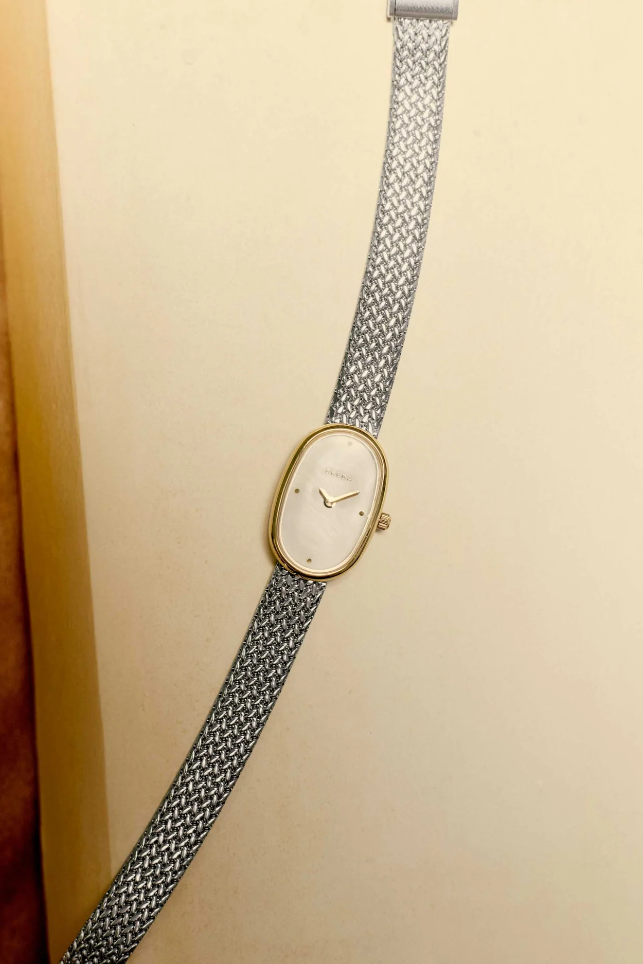 Vintage-style watch with a gold face and silver mesh strap on a beige background