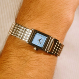 Silver watch with a blue face on a wrist against a neutral background