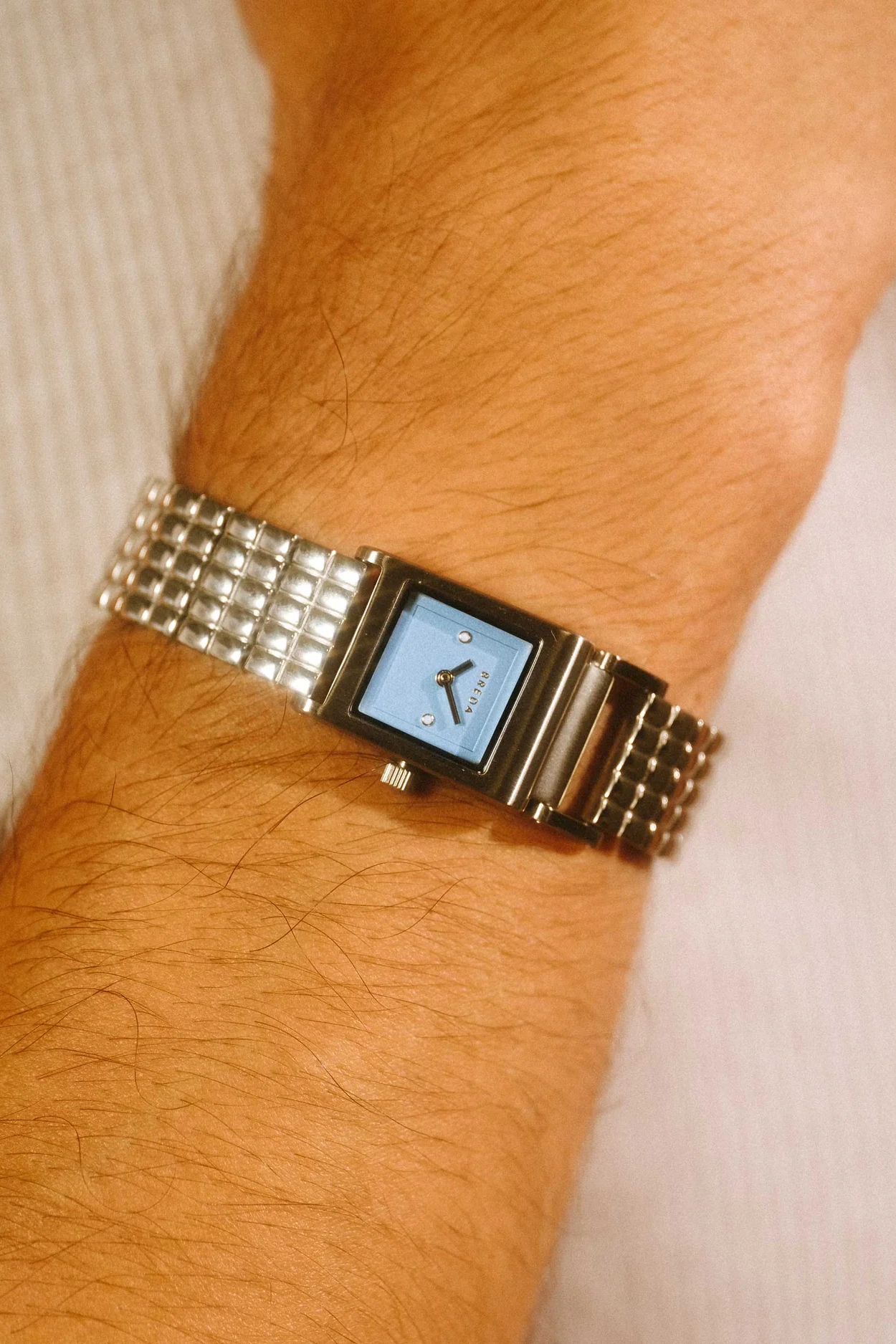 Silver watch with a blue face on a wrist against a neutral background