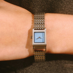 Rectangular watch with a blue face on a person's wrist against a dark background