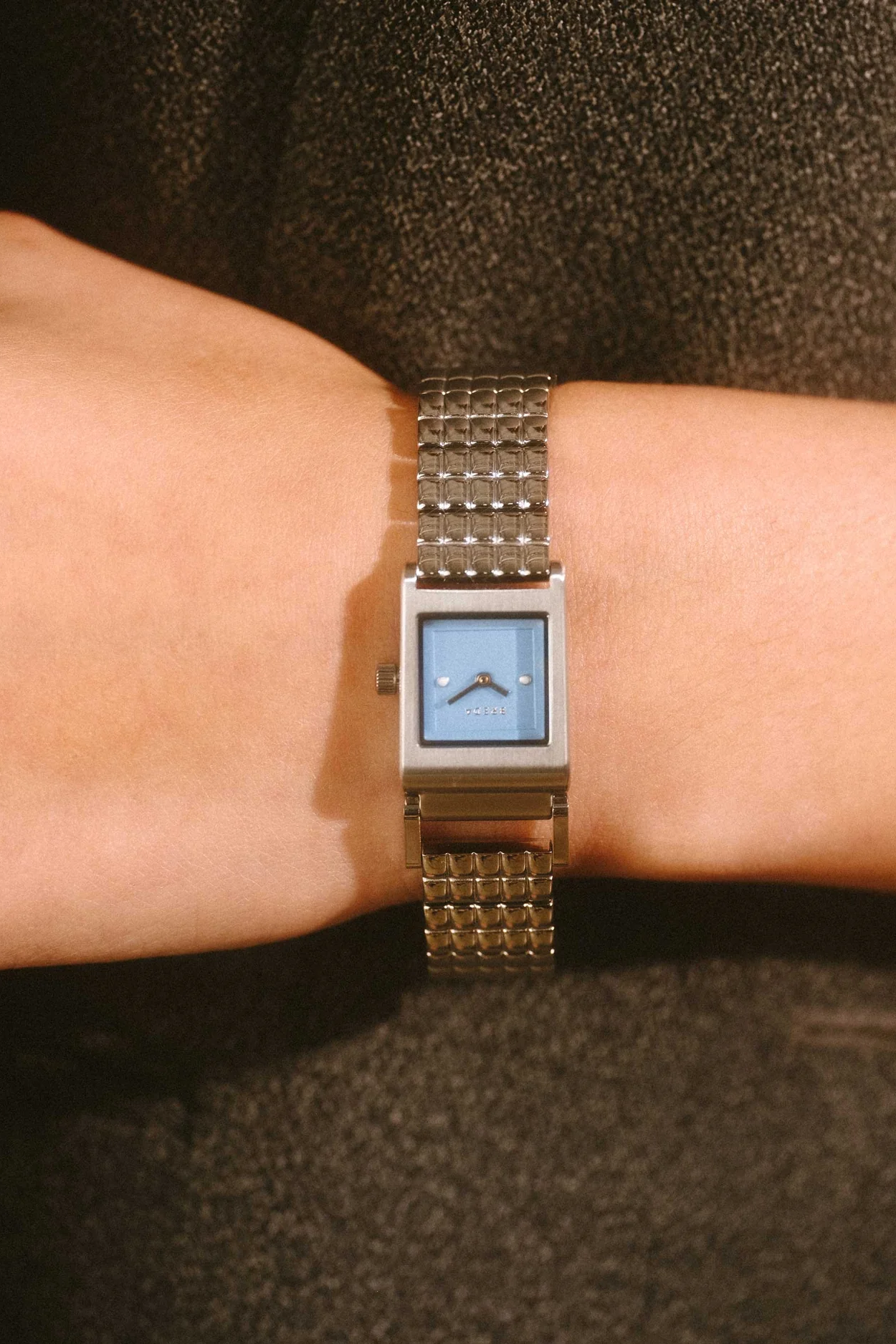 Rectangular watch with a blue face on a person's wrist against a dark background