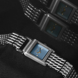 three metallic wristwatches with blue face on a textured black background