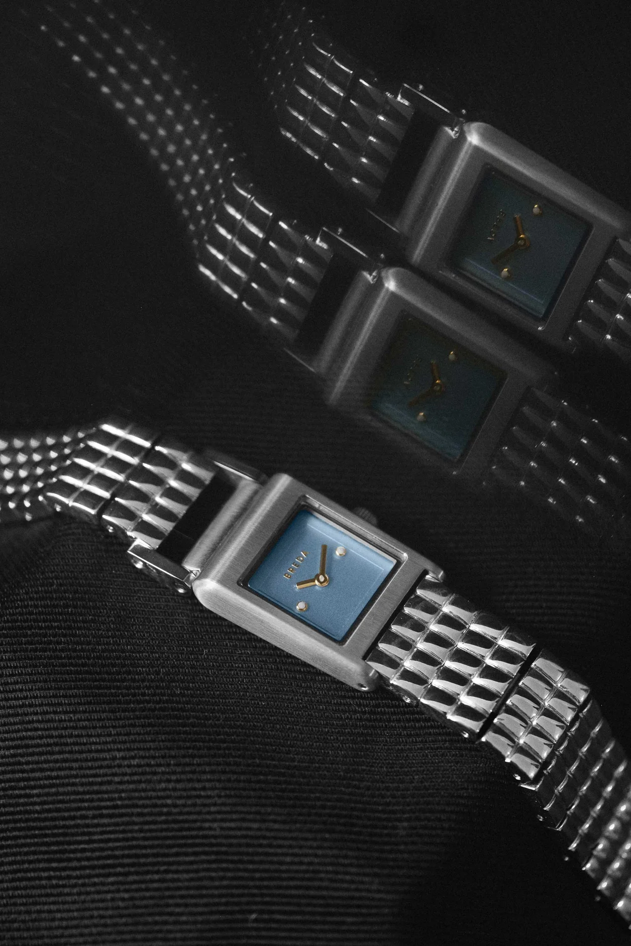 three metallic wristwatches with blue face on a textured black background