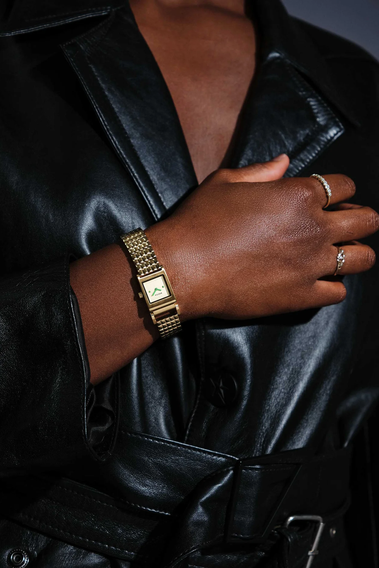 Hand wearing a gold watch and bracelet with a black leather coat