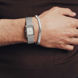 Person wearing a silver watch and bracelet on a dark background