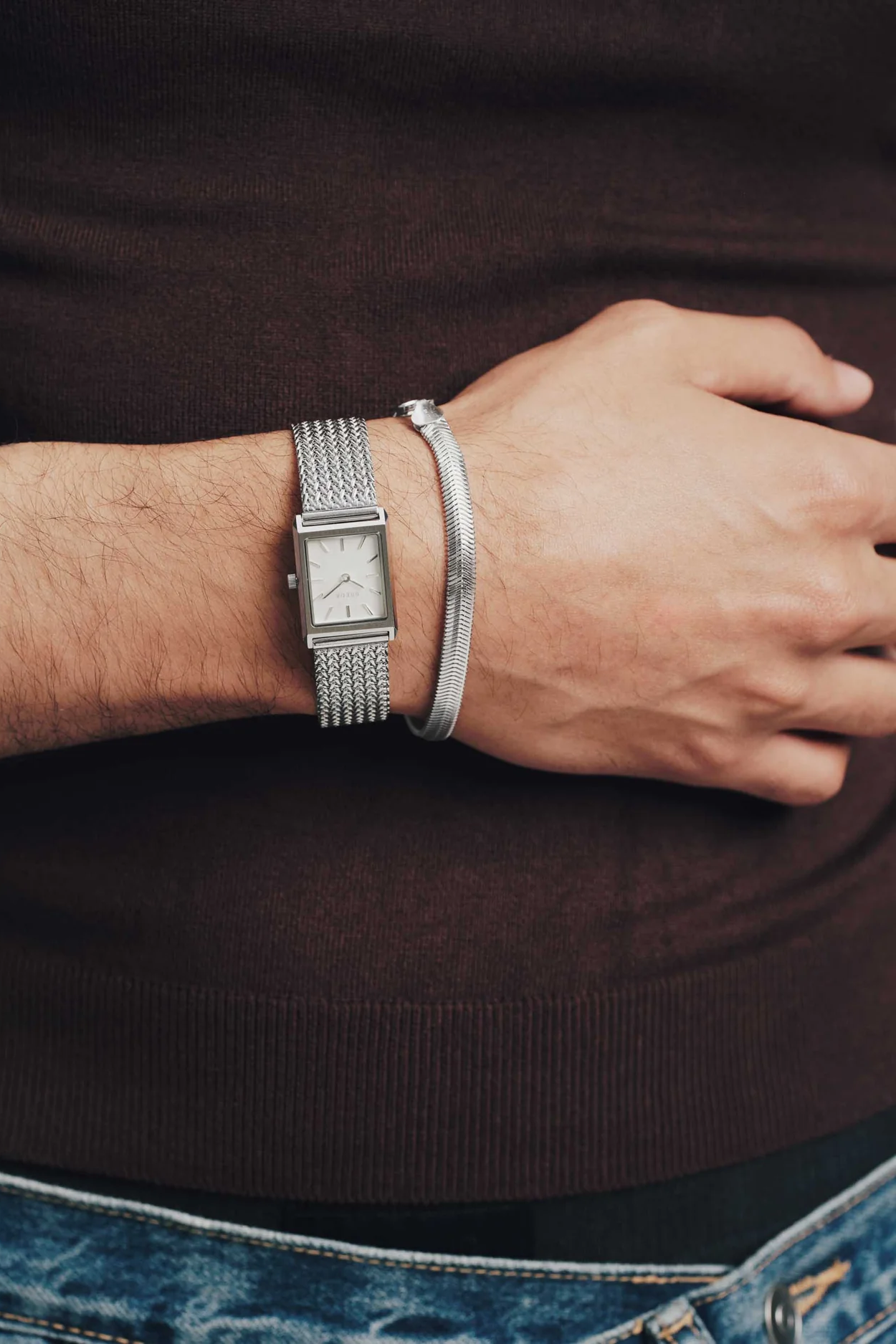 Person wearing a silver watch and bracelet on a dark background