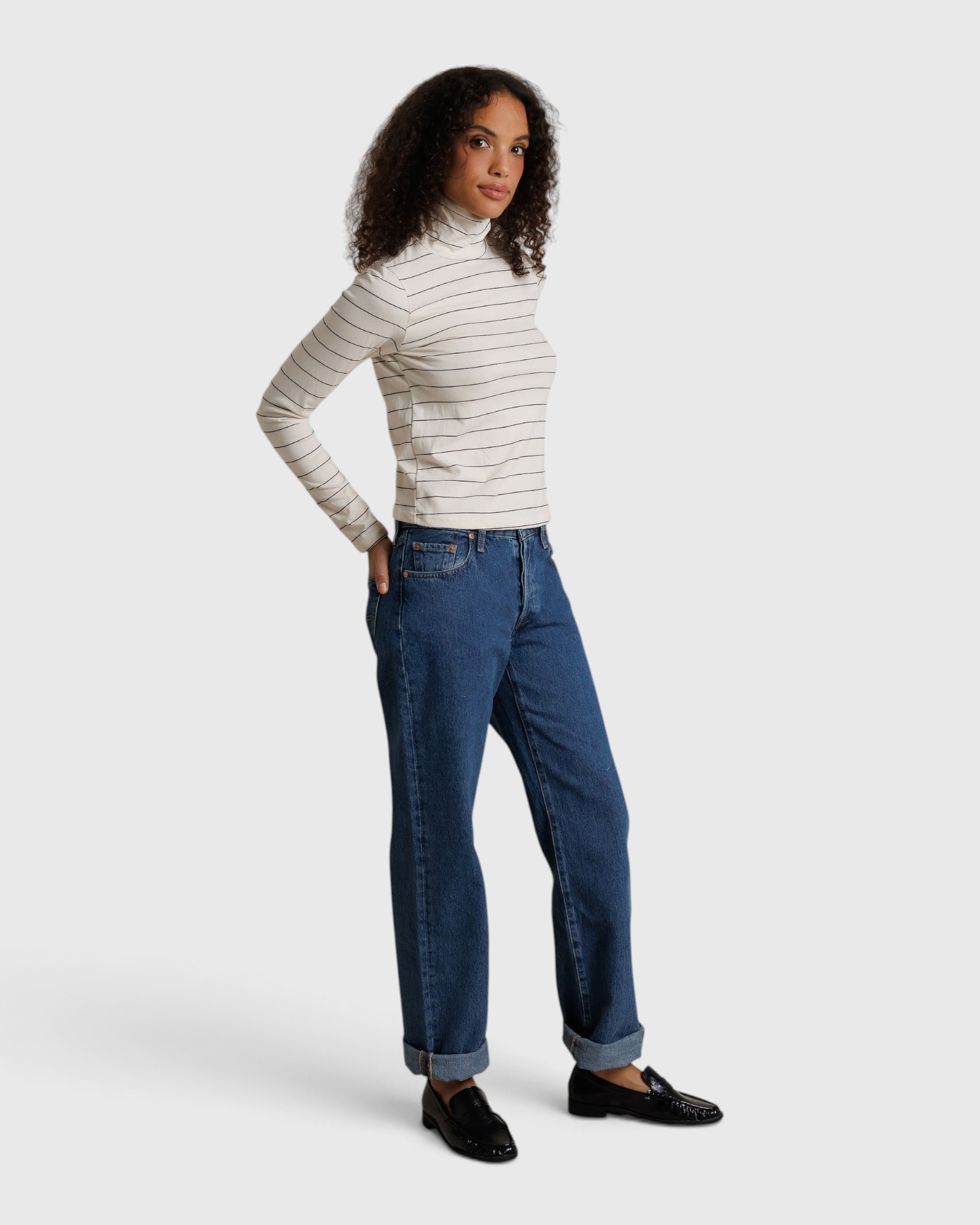 Model wearing JONES + CO Cindy long sleeve turtleneck in natural stripe with blue jeans and black loafers