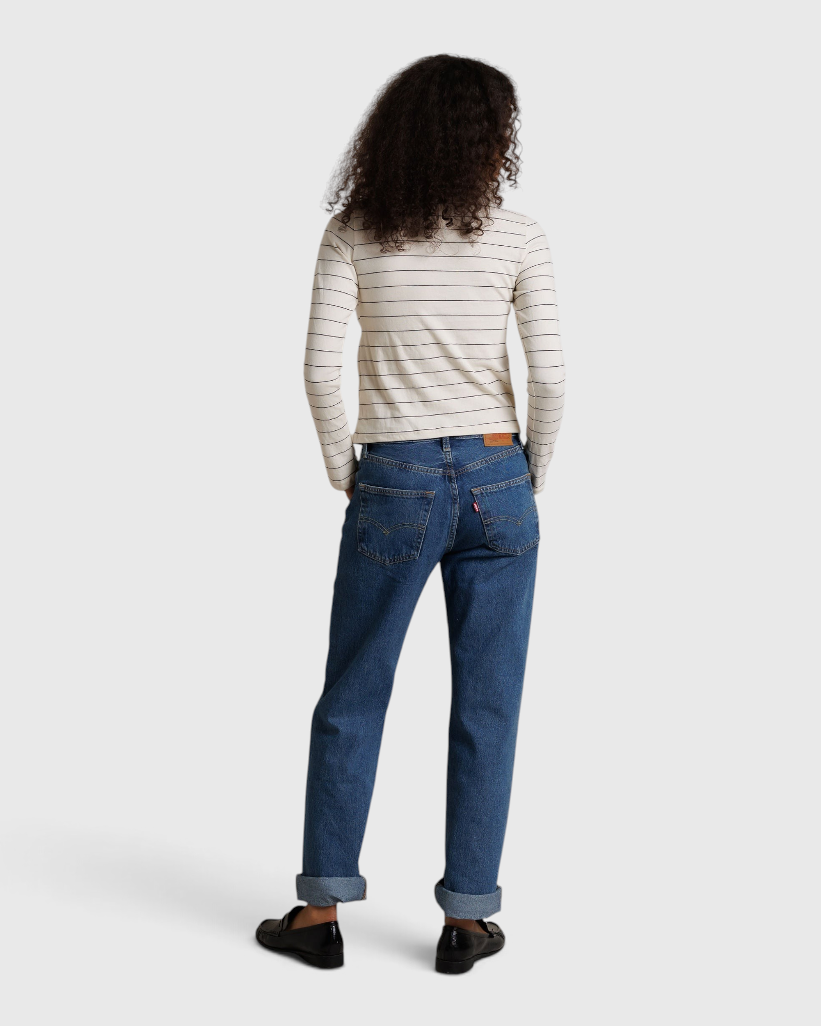 JONES + CO Cindy long sleeve turtleneck in natural stripe worn with blue cuffed jeans and black loafers, back view