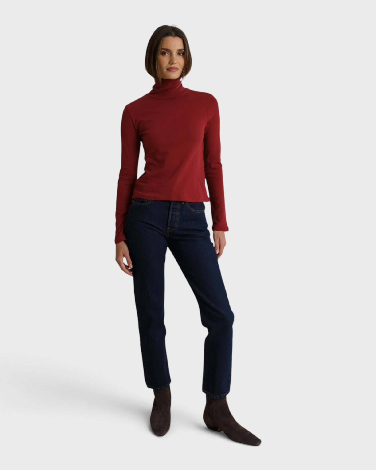 Model wearing a JONES + CO ruby red recycled cotton Cindy turtleneck paired with dark denim jeans
