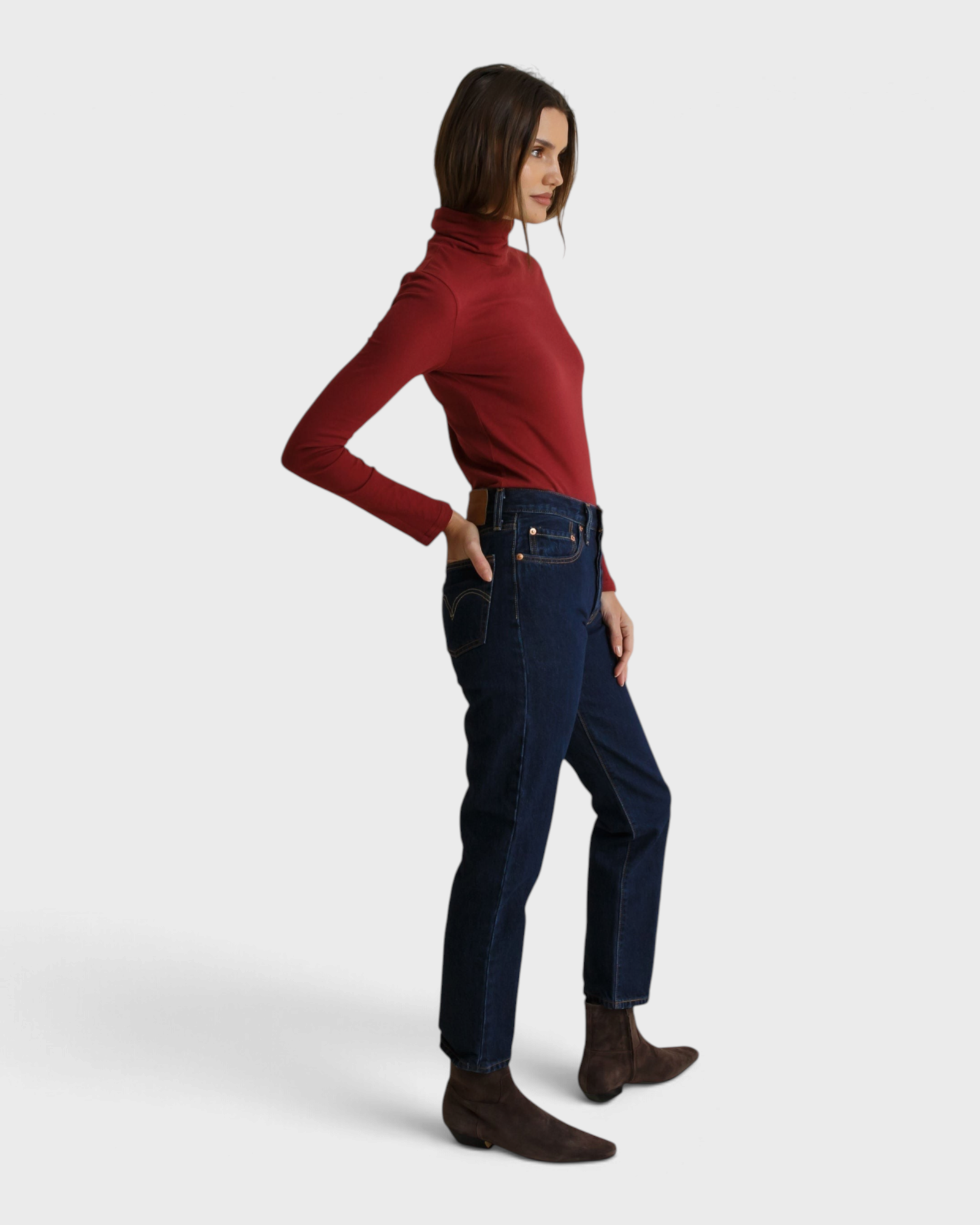 Model wearing a JONES + CO ruby red recycled cotton Cindy turtleneck paired with dark wash jeans and brown boots