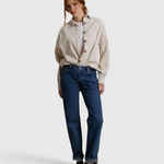 Model wearing a JONES + CO whitecap gray button-up shirt with blue jeans and brown loafers against a fabric backdrop.