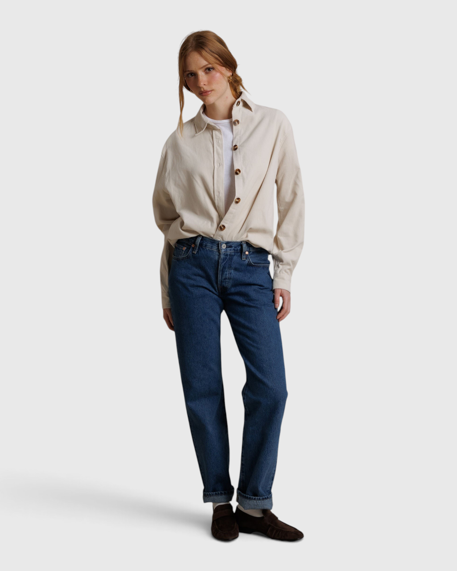 Model wearing a JONES + CO whitecap gray button-up shirt with blue jeans and brown loafers against a fabric backdrop.