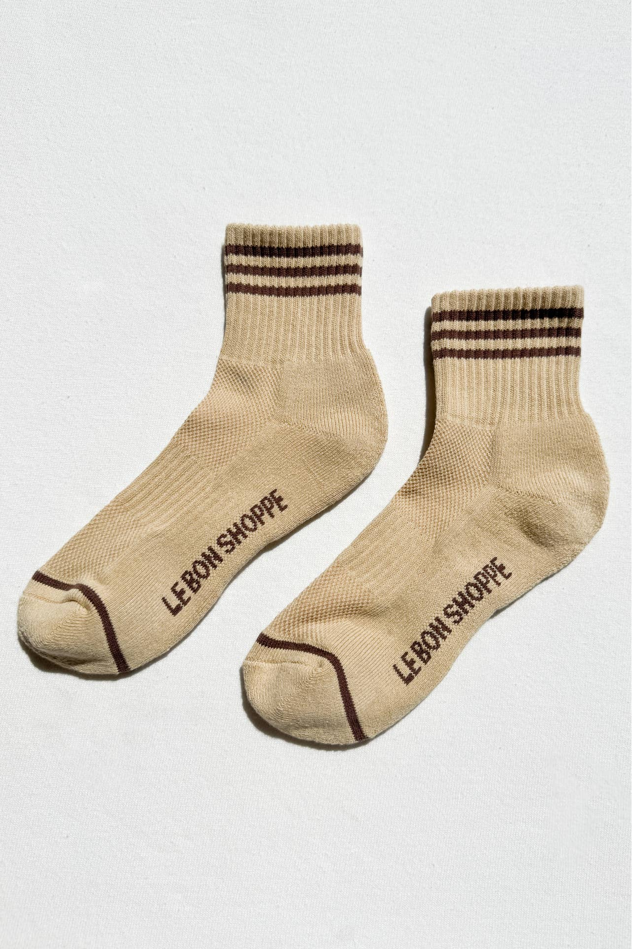 Pair of beige socks with brown stripes and 'Le Bon Shoppe' branding on a white background