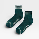 Two green socks with white stripes and 'Le Bon Shoppe' branding on a light gray background