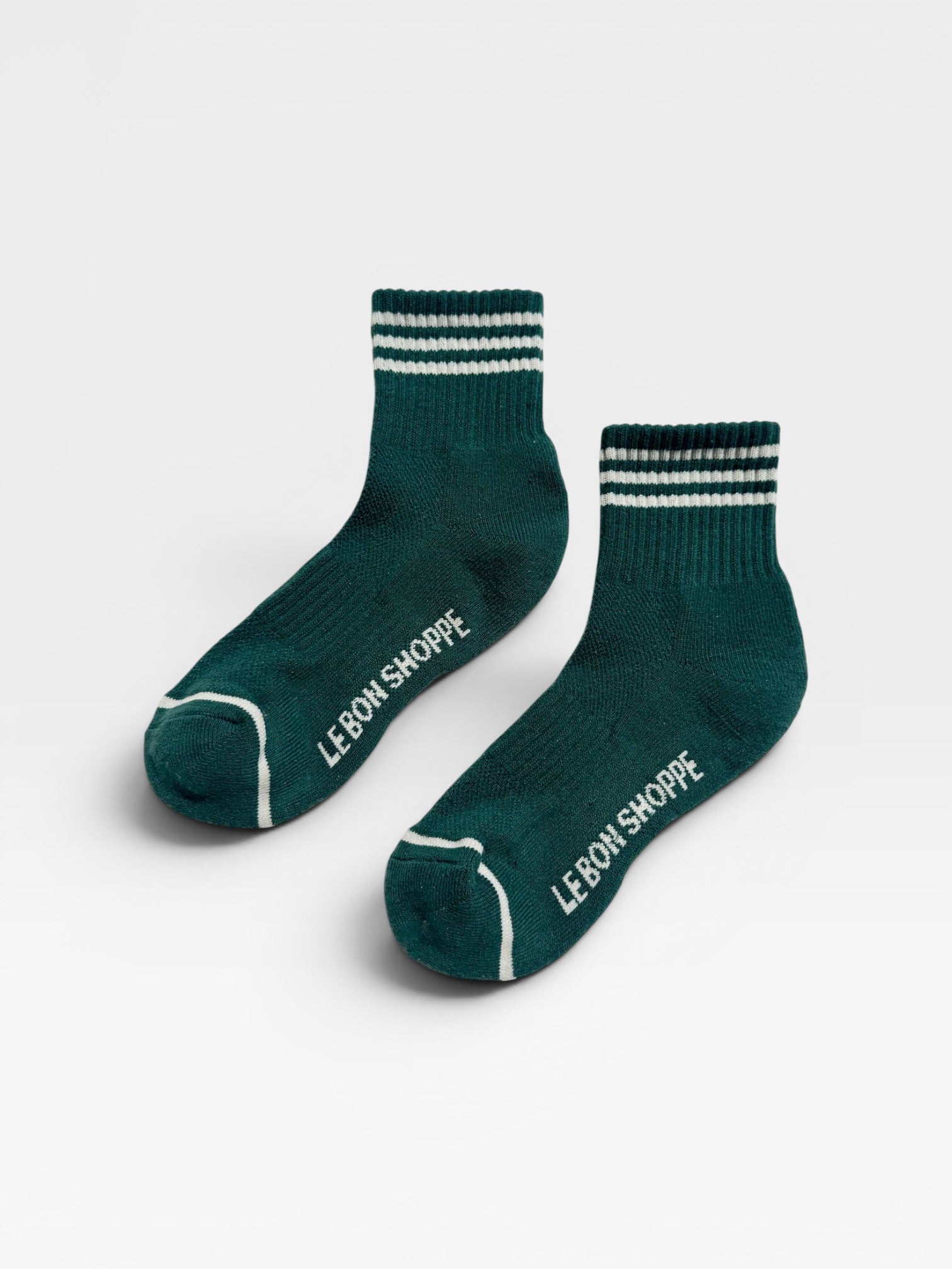 Two green socks with white stripes and 'Le Bon Shoppe' branding on a light gray background