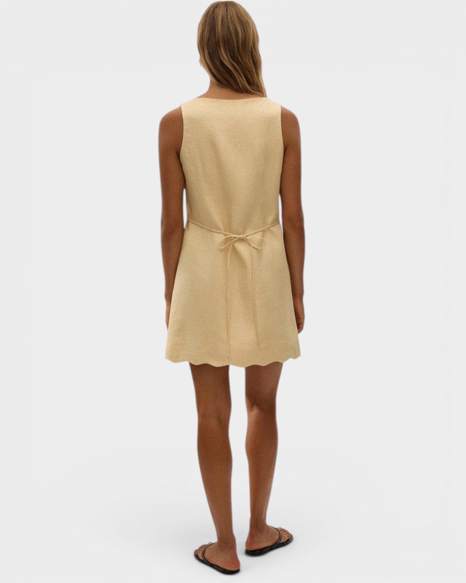 JONES + CO Alondra mini dress in daffodil yellow with a scalloped hem and tie-back detail on a model.
