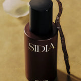 JONES + CO BRALESS body mist in a dark brown bottle with a black cap, set against a warm, textured gold background.