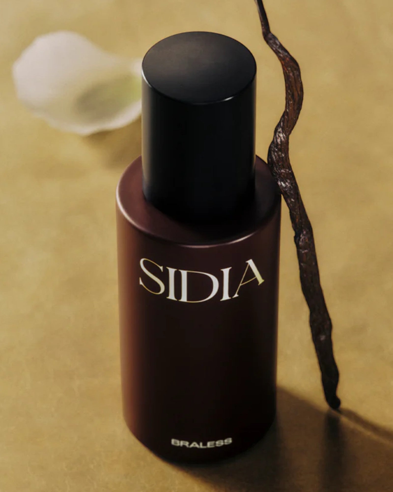 JONES + CO BRALESS body mist in a dark brown bottle with a black cap, set against a warm, textured gold background.