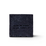 JONES + CO charcoal and lavender soap brick with Made by Hand in Los Angeles embossed on a black textured surface.