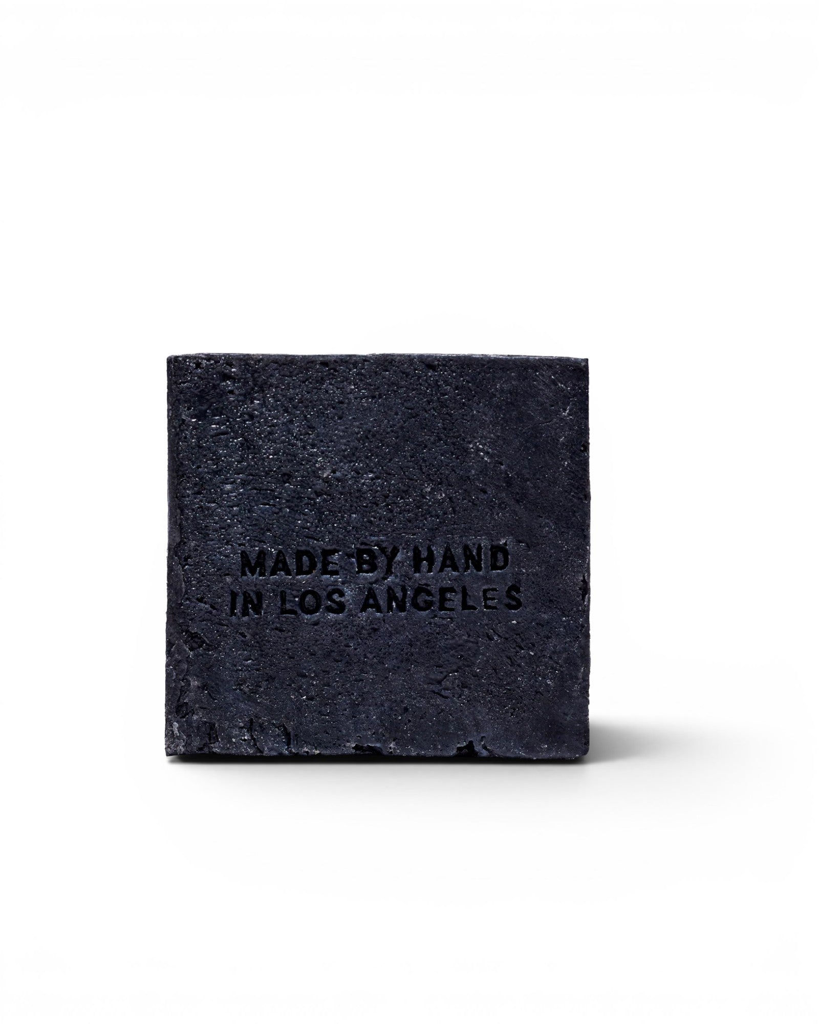 JONES + CO charcoal and lavender soap brick with Made by Hand in Los Angeles embossed on a black textured surface.