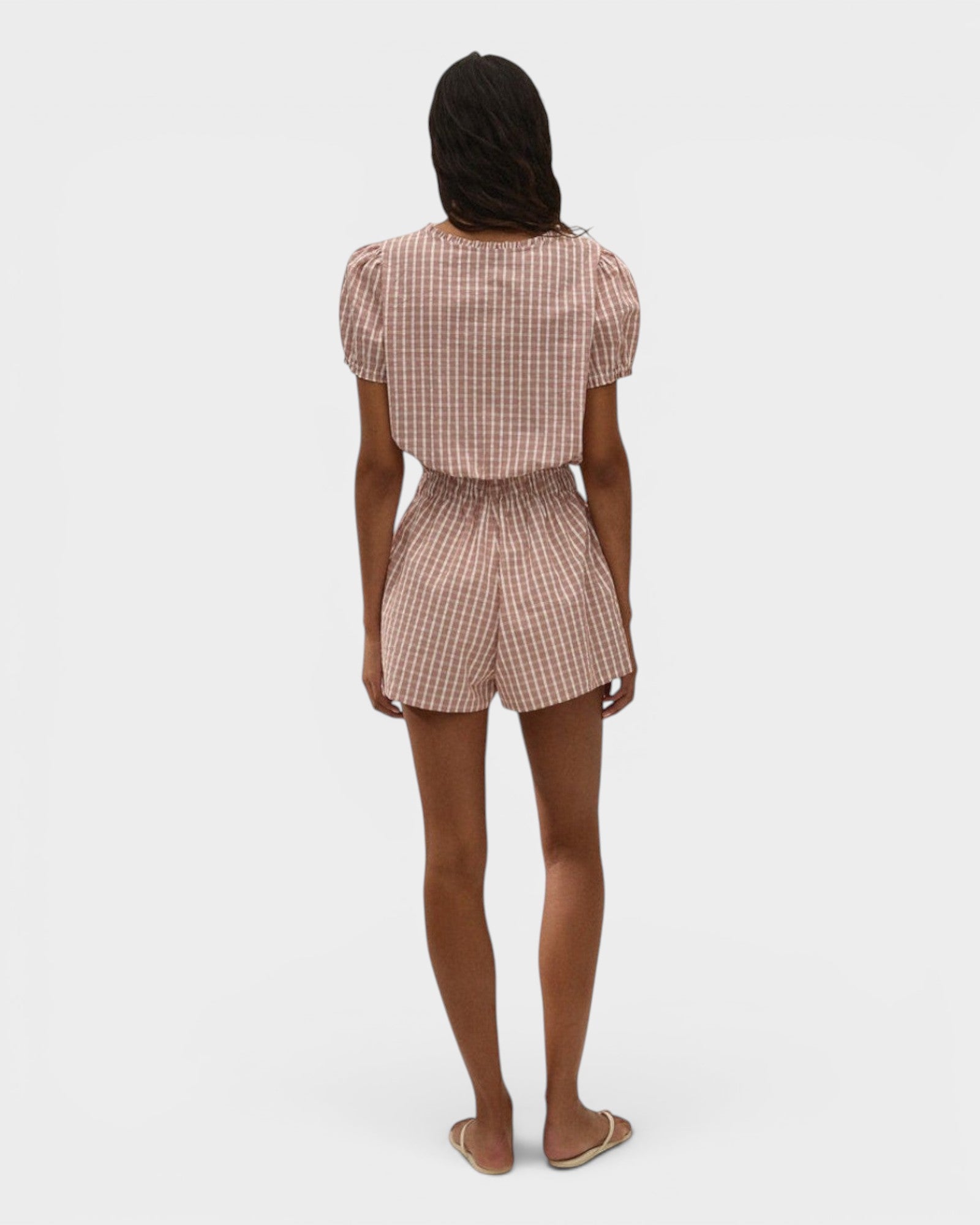 Back view of a model wearing JONES + CO Emilie playsuit in cinnamon and white gingham check with puff sleeves.